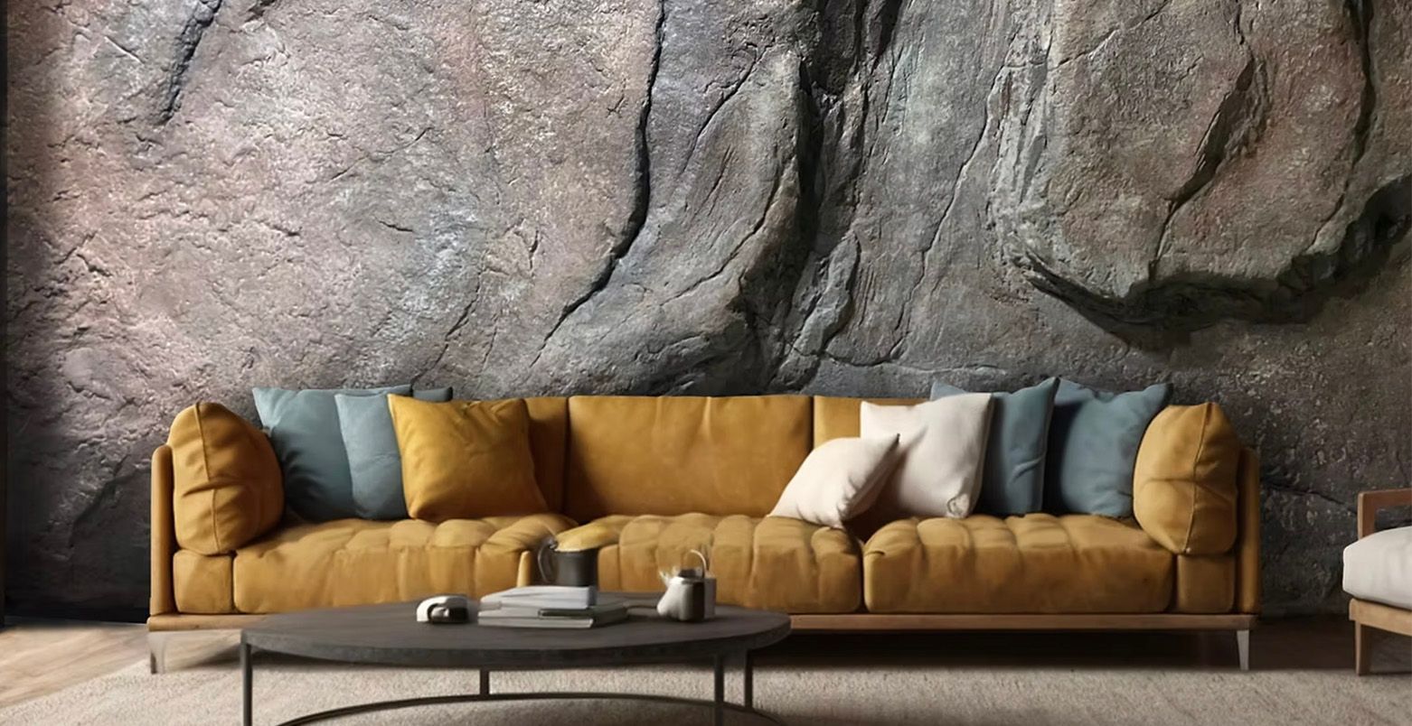 Mustard yellow sofa against a gray stone wall, with blue and white pillows, and a black coffee table.