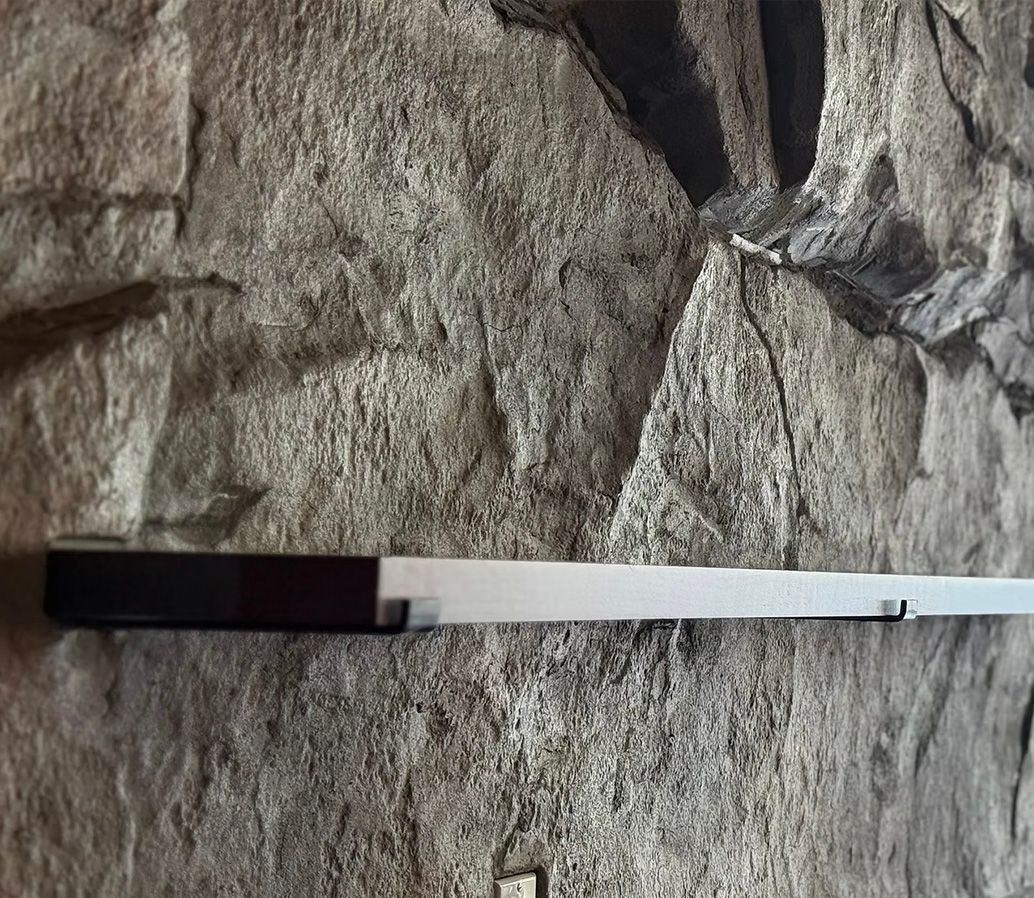 Black and silver lightsaber resting horizontally against a textured gray rock wall.