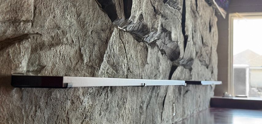 A long, white shelf is mounted on a rough stone wall near a window.