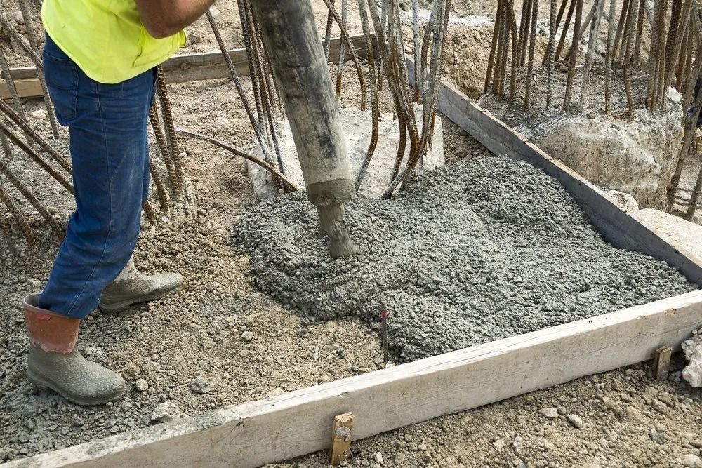 Concrete being poured from a hose into a wooden formwork frame at a construction site.