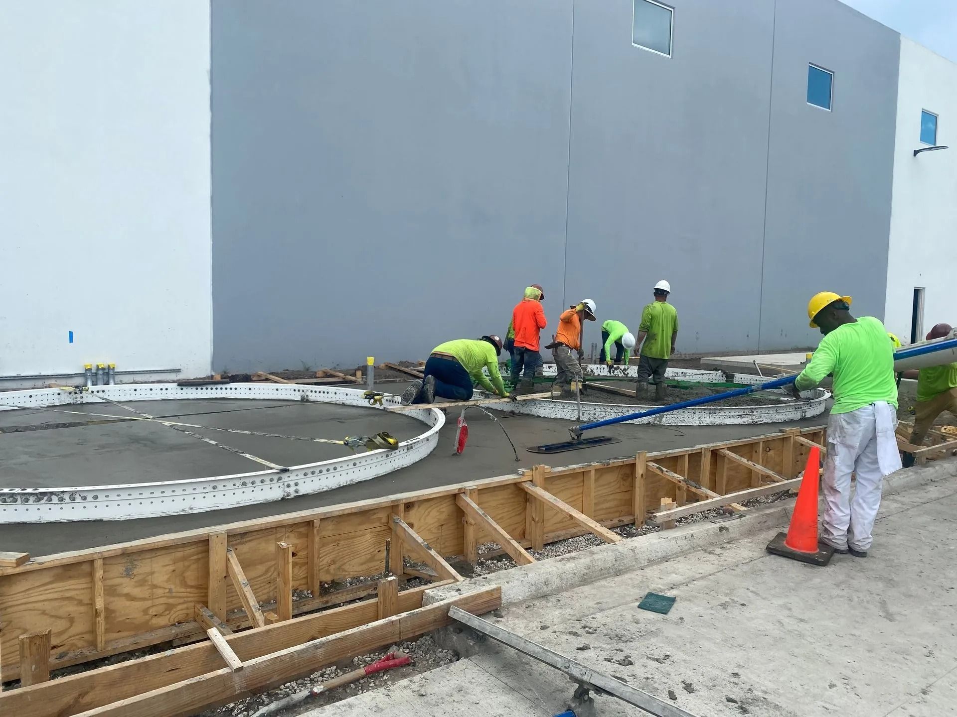 Construction crew in high-visibility vests finish a concrete surface next to a large building wall.