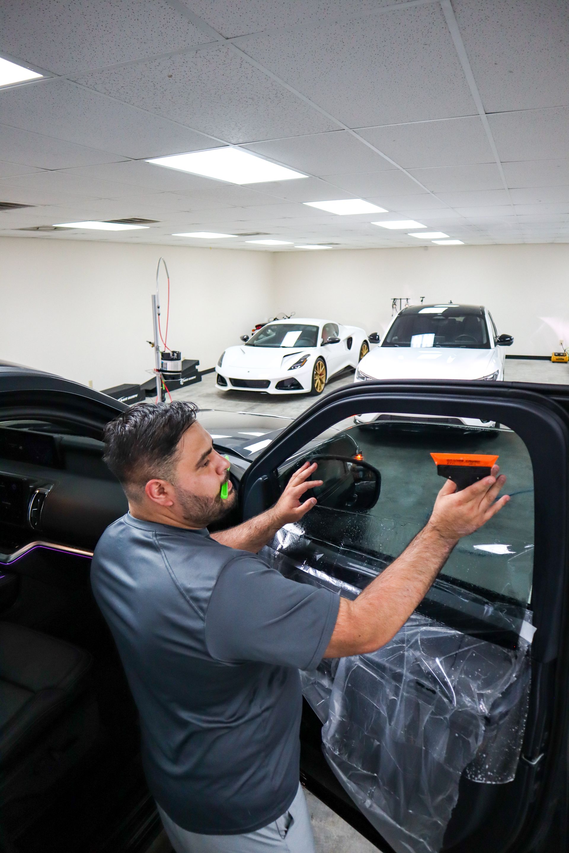 Man applying tint to car window in a garage, with two cars in the background.