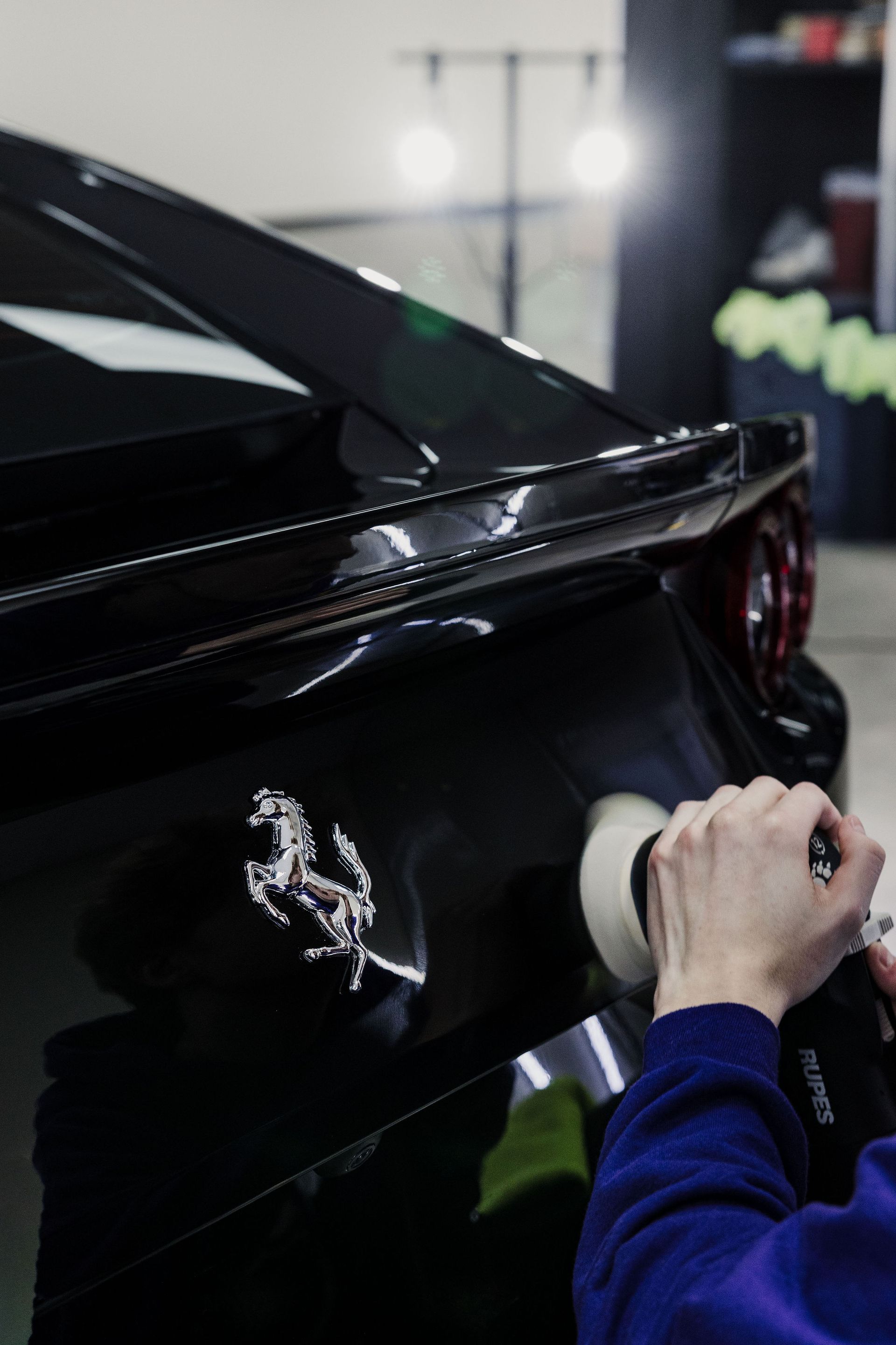 A person polishing a black Ferrari's side near the logo.