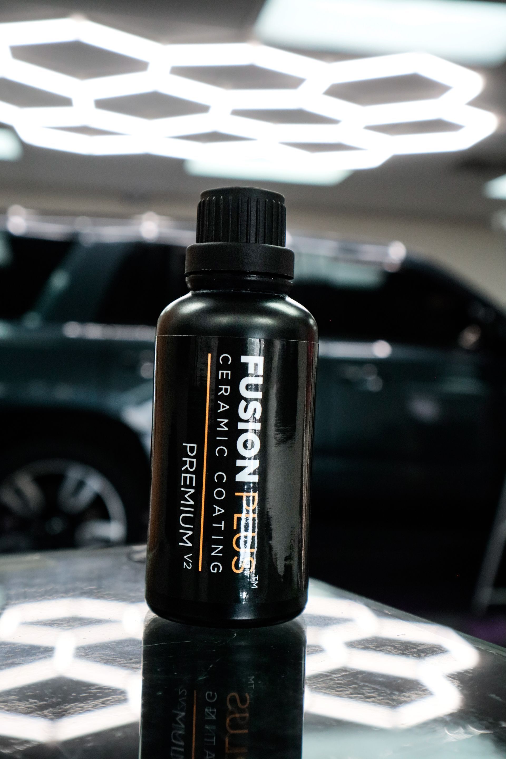 Black bottle of Fusion Plus ceramic coating in a well-lit garage setting, with a dark green SUV in the background.