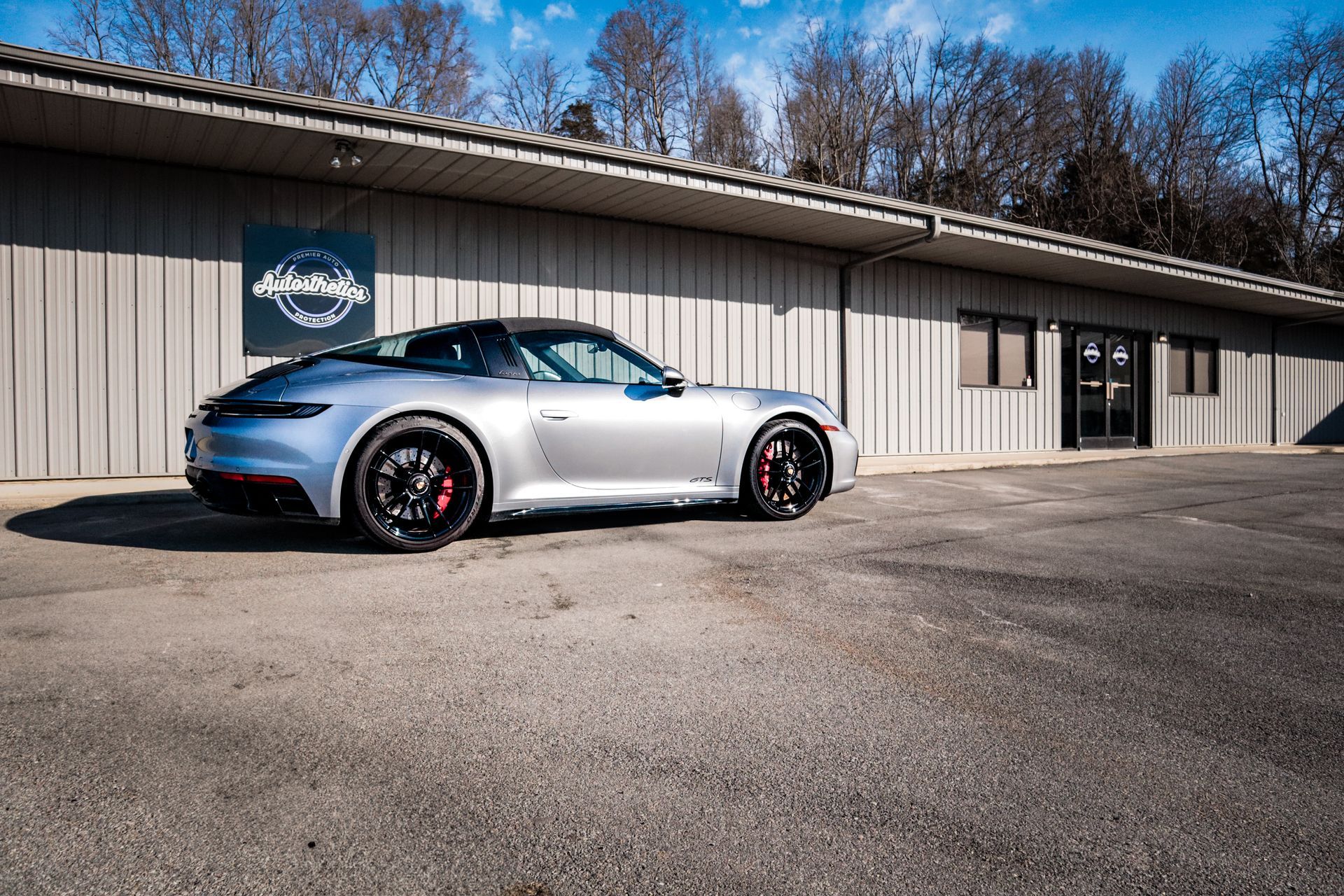 A silver porsche 911 is parked in front of a building.