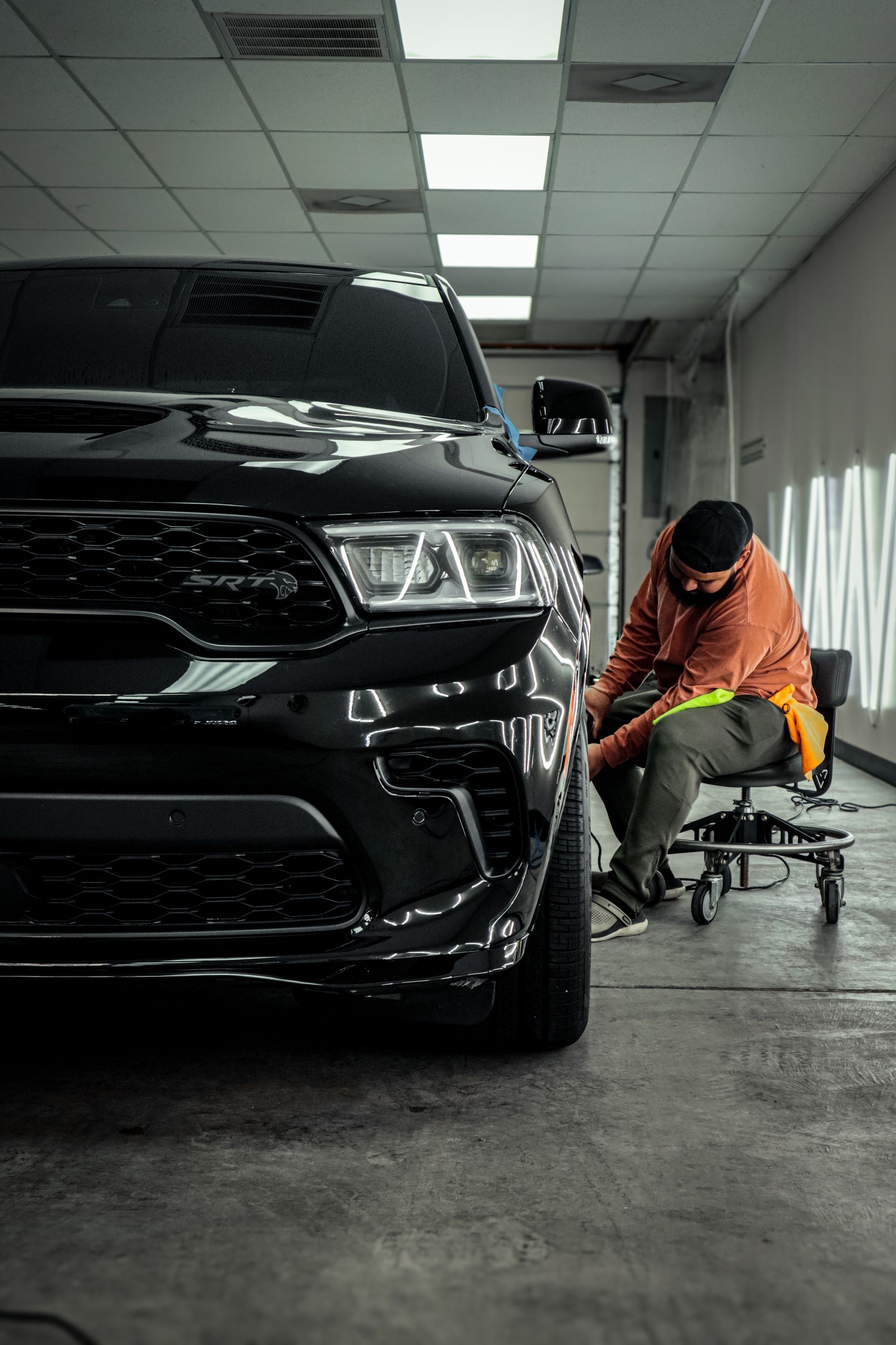 A person working on a black SUV in a garage, polishing the side.