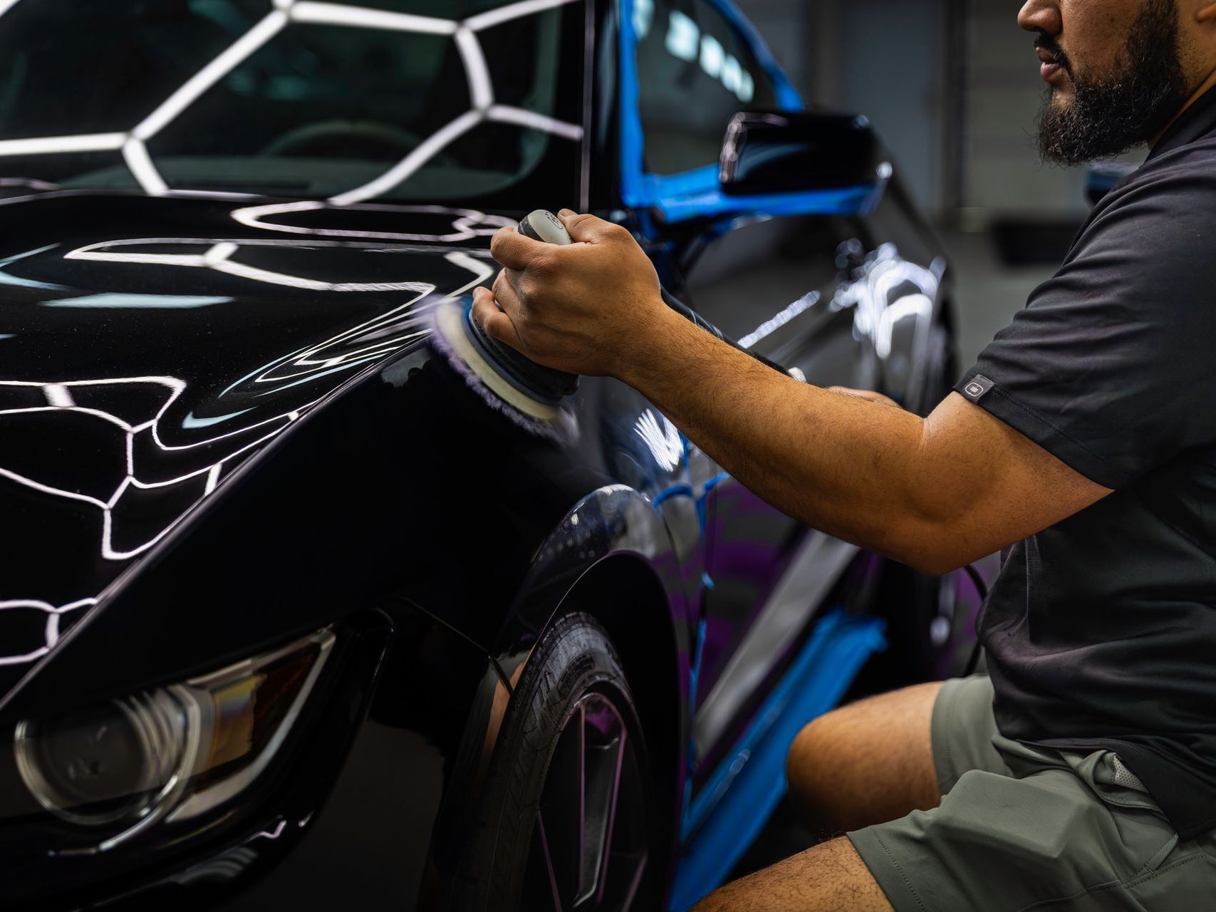 A man is polishing a white car with a machine.