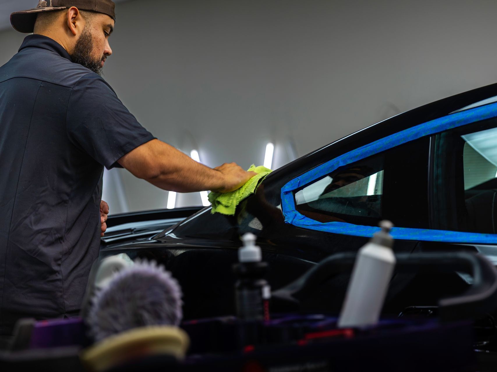 A man is cleaning a car with a cloth in a garage.