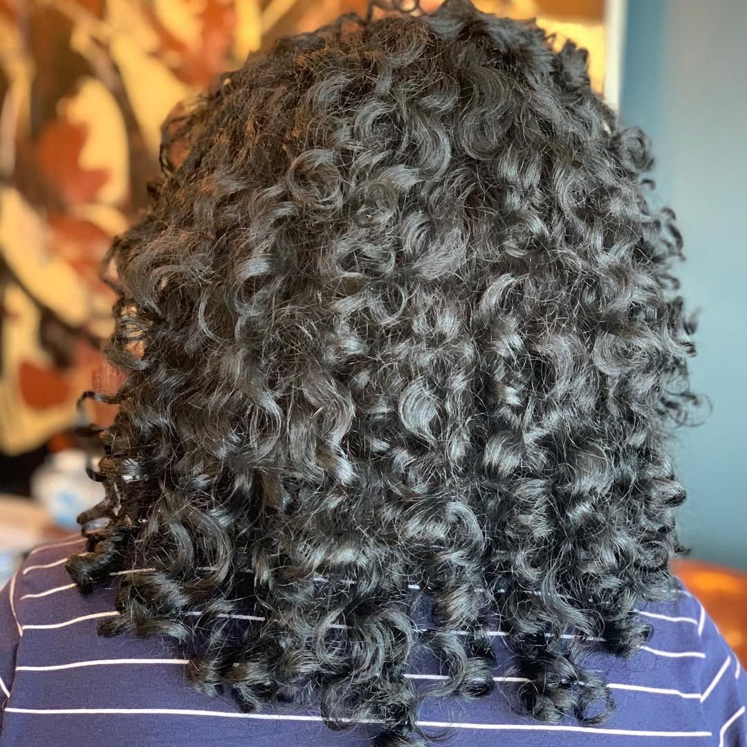 Back view of dark, curly hair over a person wearing a striped shirt.