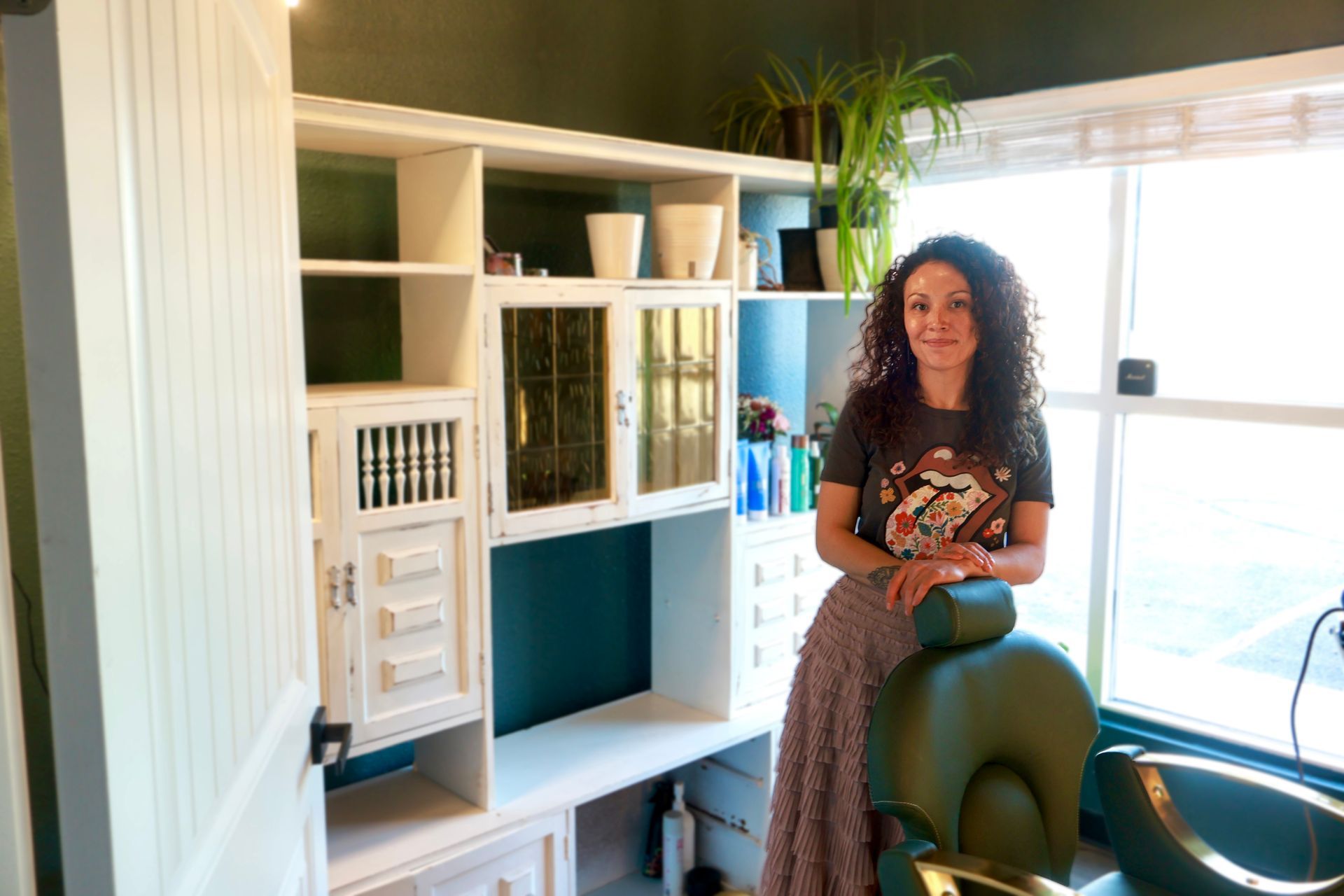 Woman stands in a beauty salon, near green chair and white cabinetry.