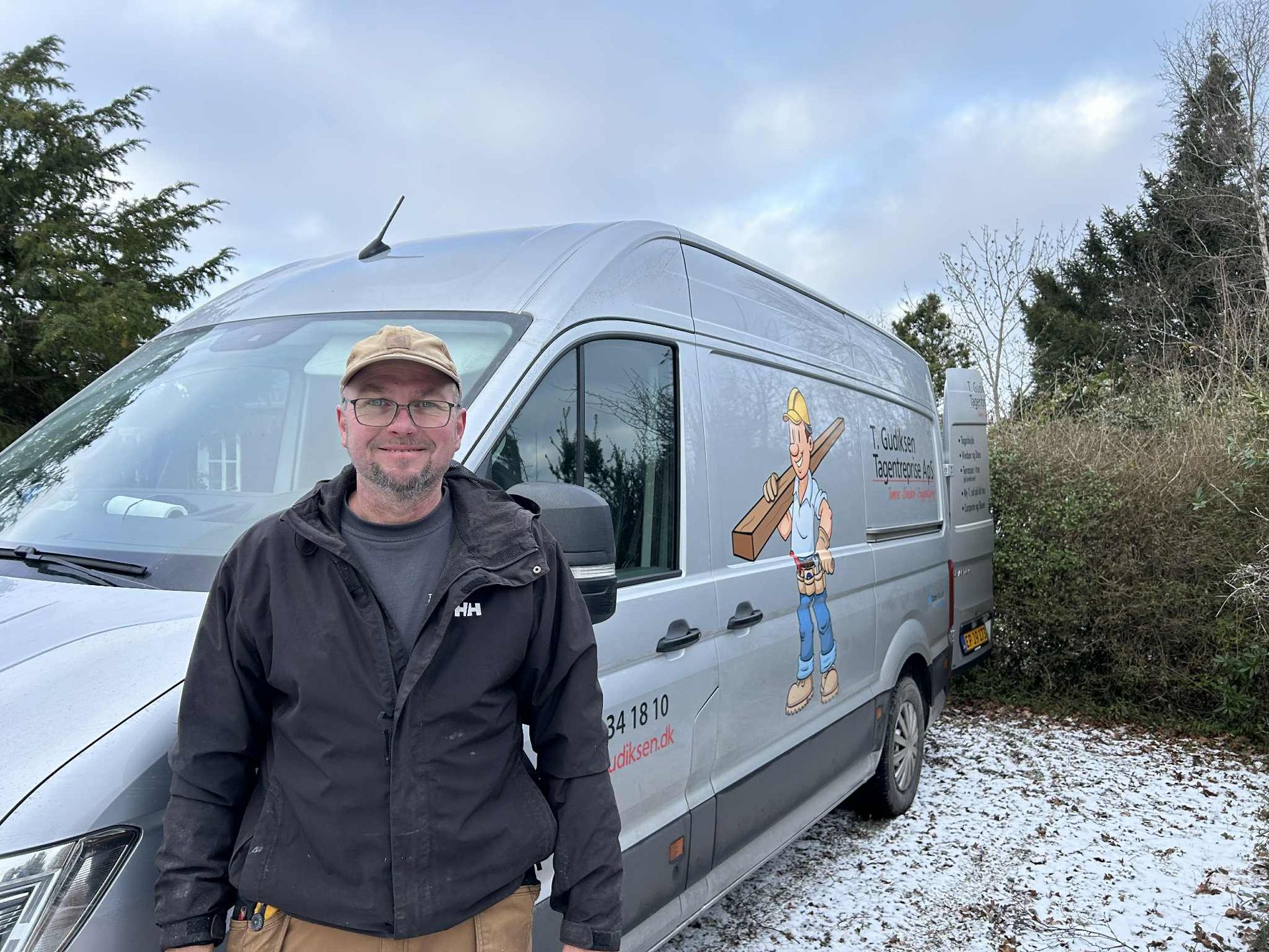 Mand foran en sølvfarvet varevogn med tegneseriefigur på, sne på jorden.