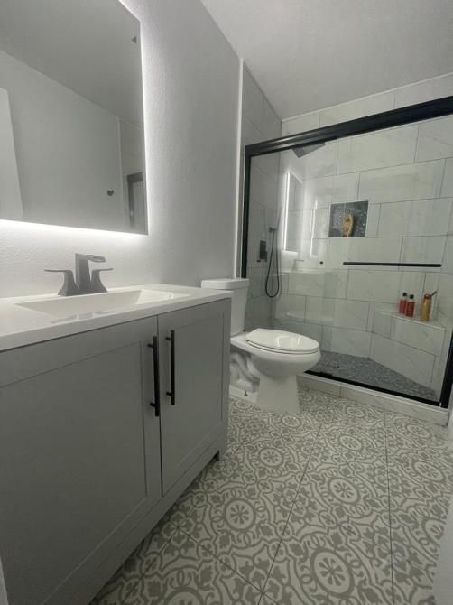 A bathroom with a toilet , sink , mirror and shower.