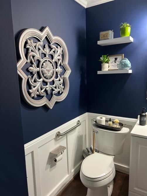 A bathroom with blue walls , a toilet , and a clock on the wall.