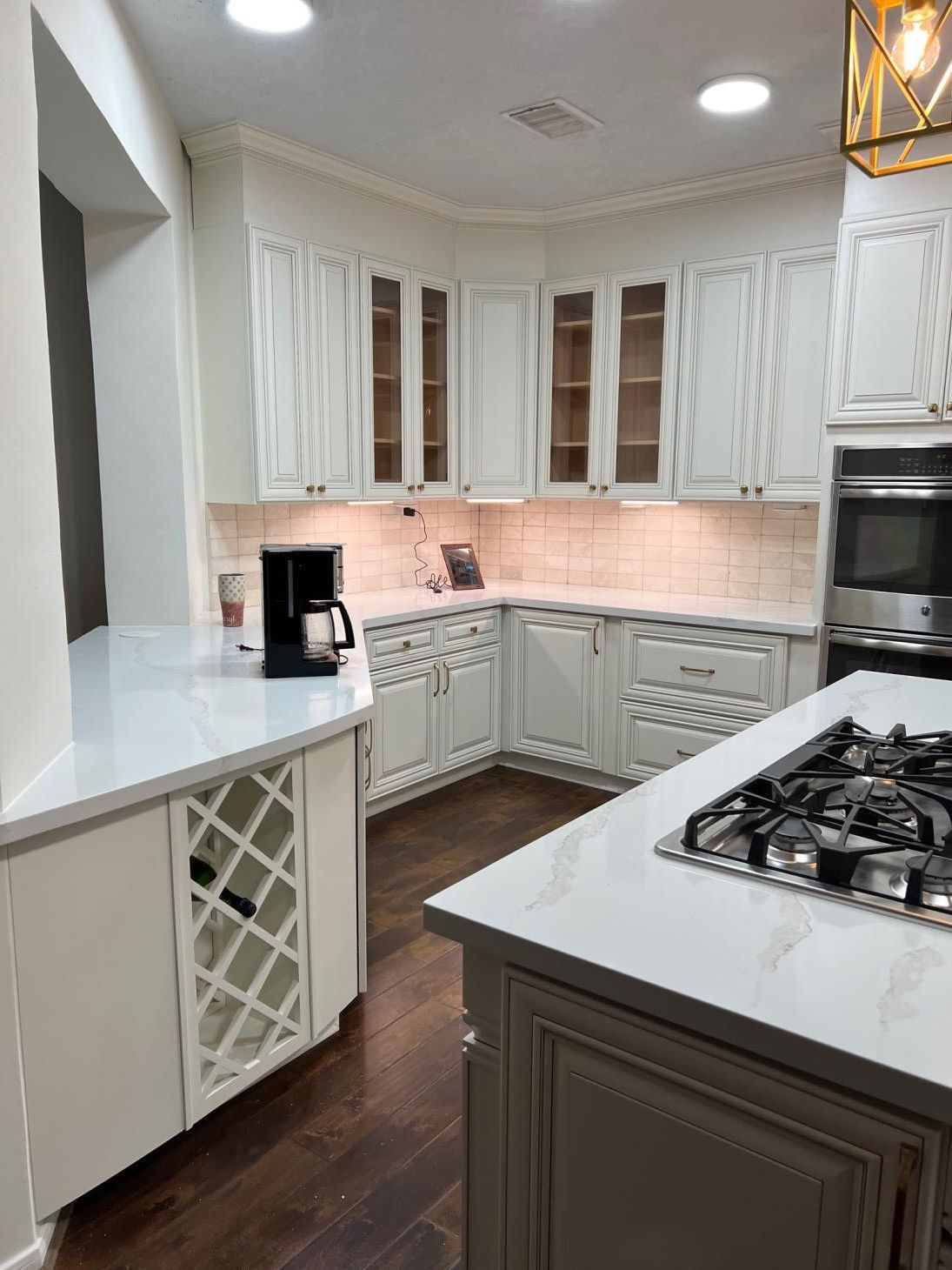 A kitchen with white cabinets , a stove top oven , a coffee maker , and a wine rack.