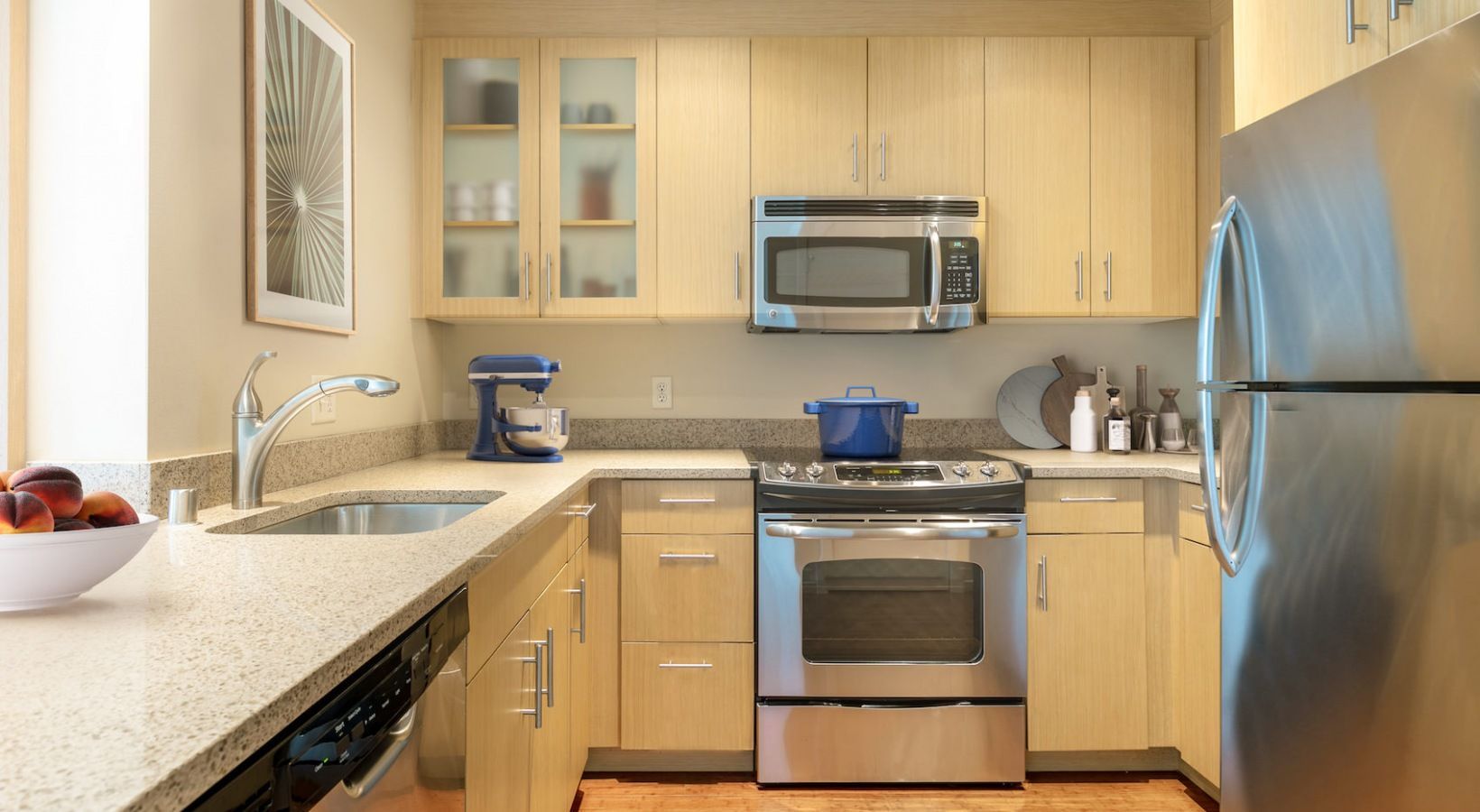 Modern apartment kitchen with stainless steel appliances, light wood cabinets, and granite countertops.