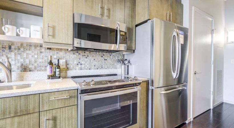 Modern kitchen with stainless steel fridge, stove, microwave, and tile backsplash.
