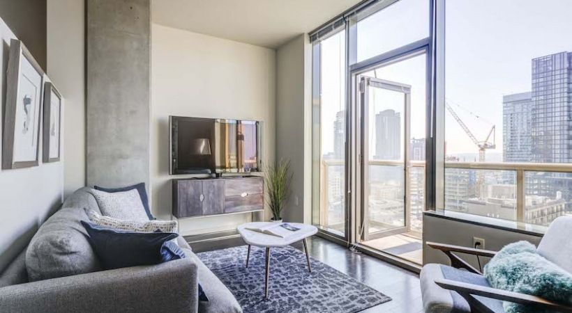 Modern living room in a high-rise apartment with large glass doors to a balcony and city views.