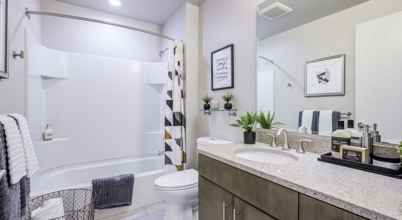 Modern apartment bathroom with tub/shower, vanity, mirror, and towels.