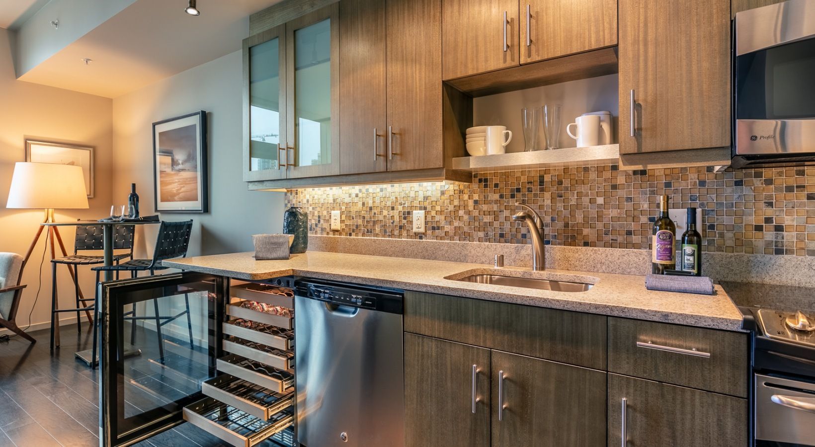 Modern apartment kitchen with wood cabinets, granite countertop, stainless appliances, and a wine fridge.