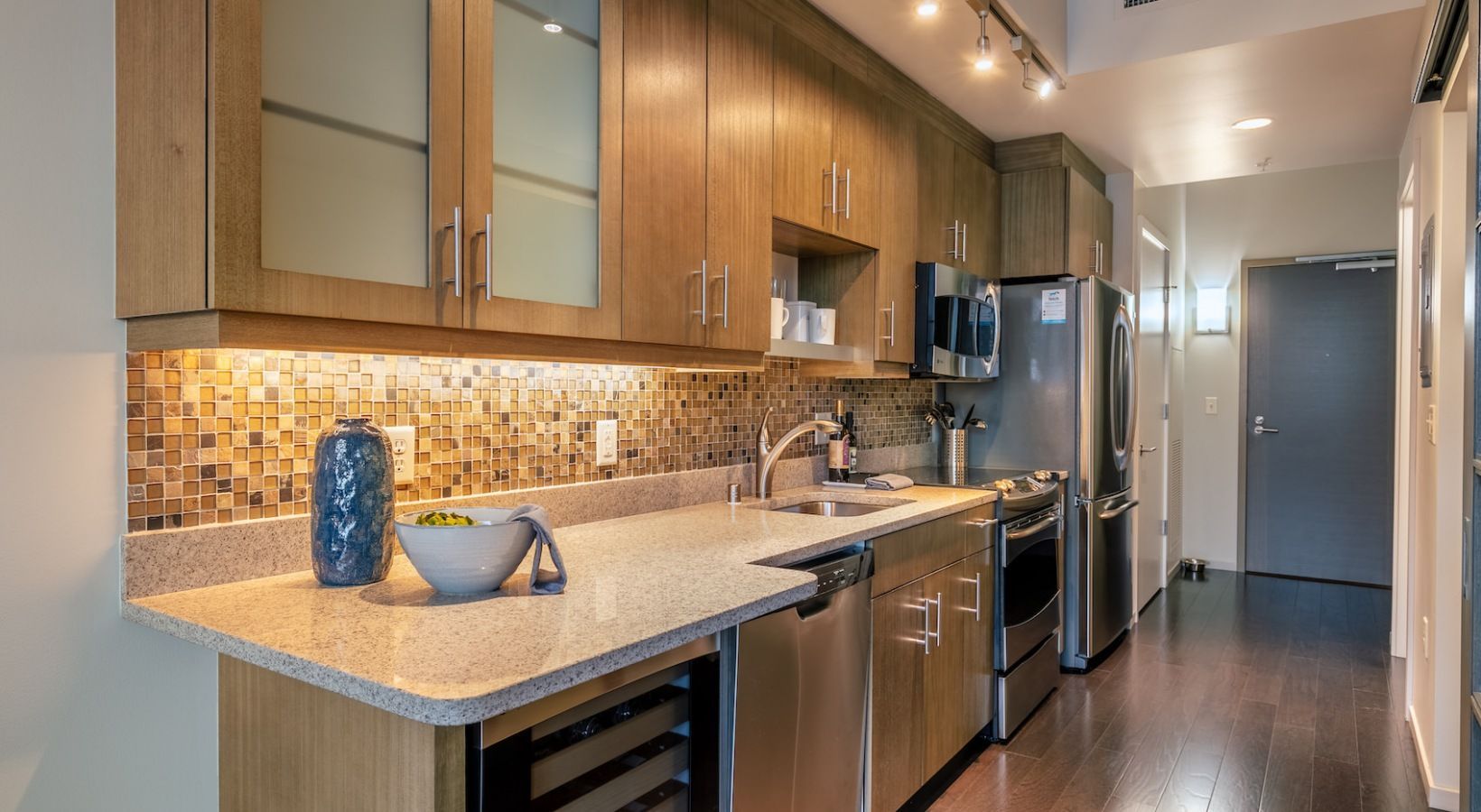 Modern galley kitchen with wood cabinets, stainless appliances, and a tiled backsplash.