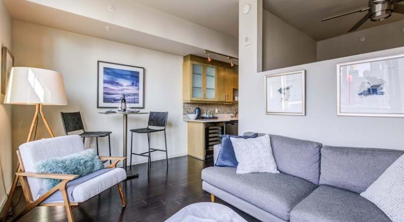Open-concept living area with a gray sofa, chair, and compact kitchen.