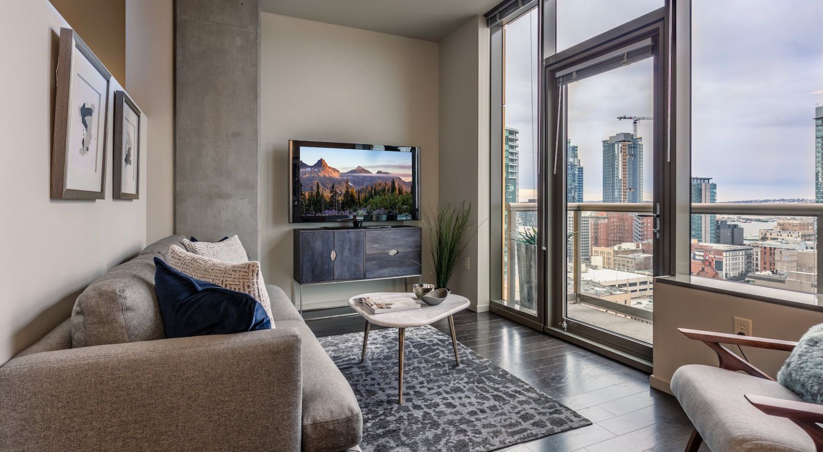 Modern living room with a sofa, TV, coffee table, and large glass doors to a city view.
