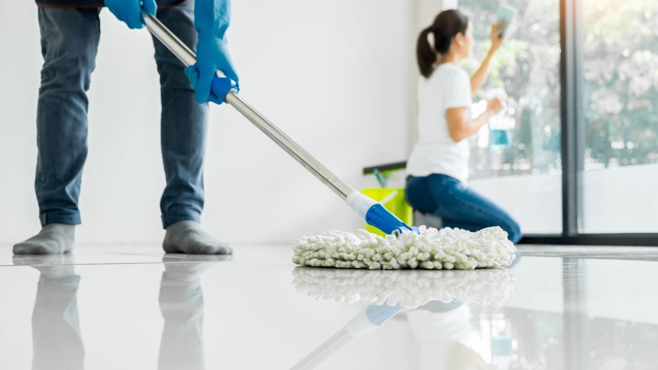 A woman and man cleaning a floor with a mop.