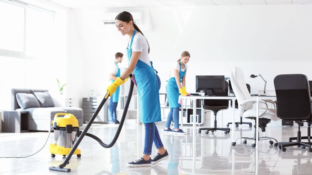 Three people using vacuum cleaners to clean an office space.