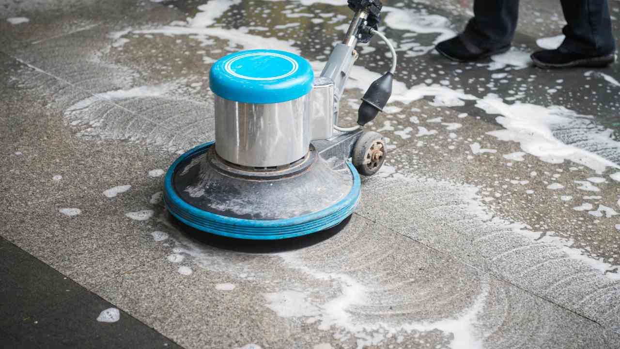 A person is cleaning a tiled floor with a machine.