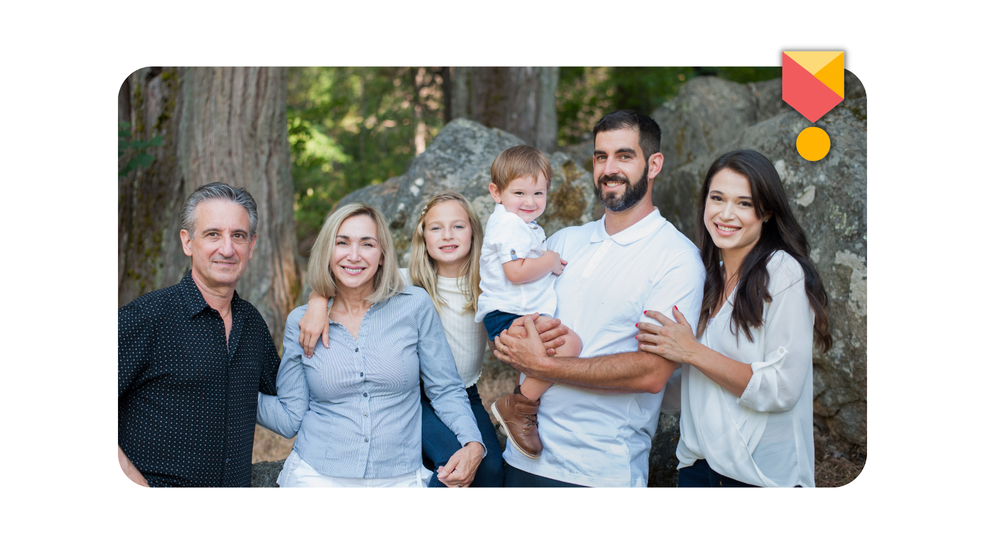 Family of six smiling, posing outdoors by trees and rocks.