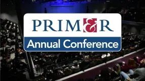 A logo for the PRIM&R Annual Conference overlaid on a blurred view of a large audience in a theater.