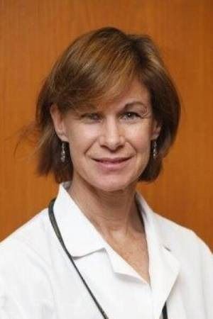 A medical professional wearing a white coat and a stethoscope against a wood-paneled background.