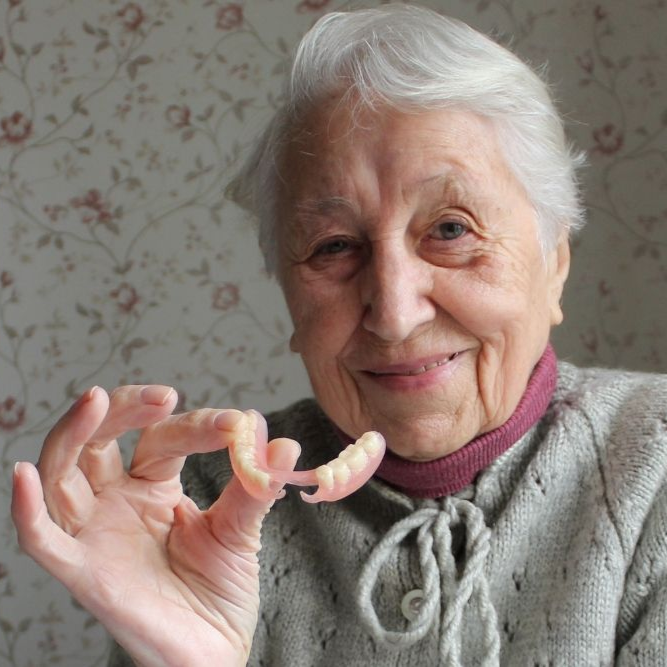 Woman holding dentures, smiling.