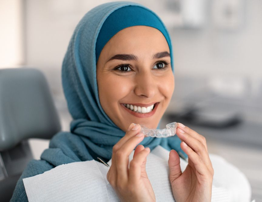 Person inserting clear aligner into mouth. Pink lipstick. White background.