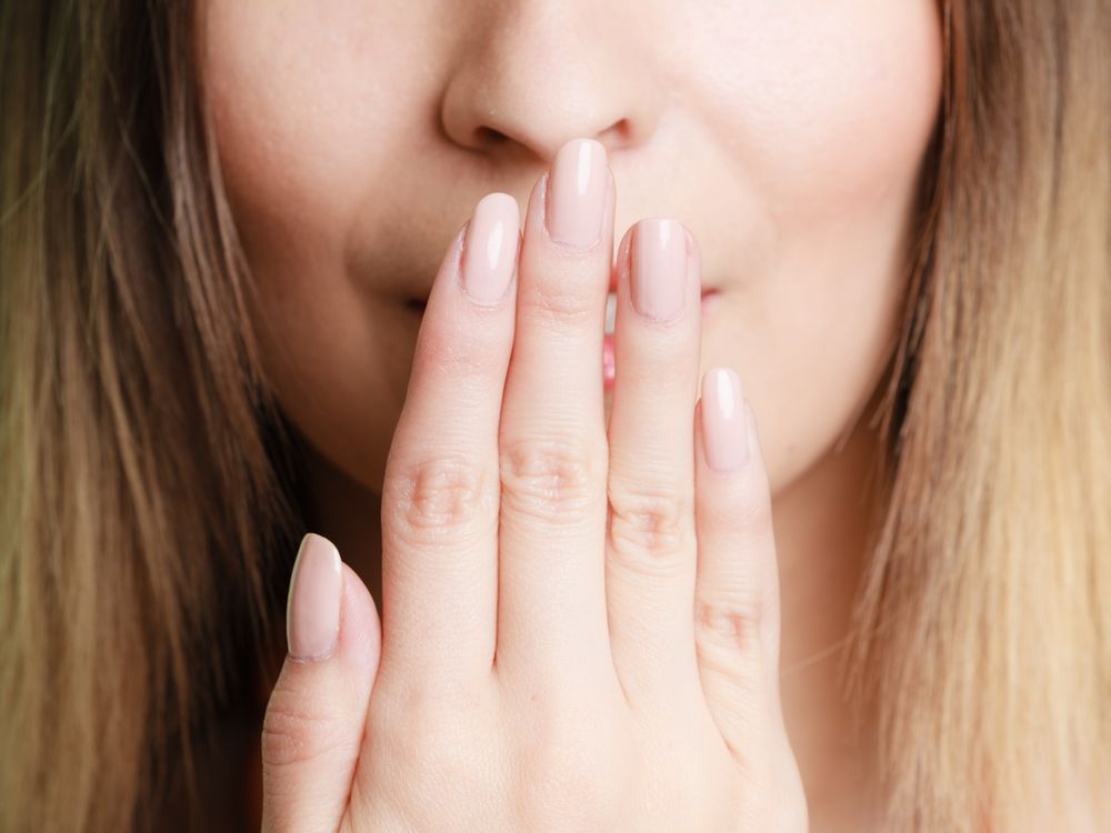 Woman covering mouth with hand, light pink nails, soft focus, indoor.
