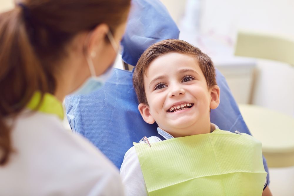 Boy smiling at a dentist wearing a mask and examining tools in a dental office.
