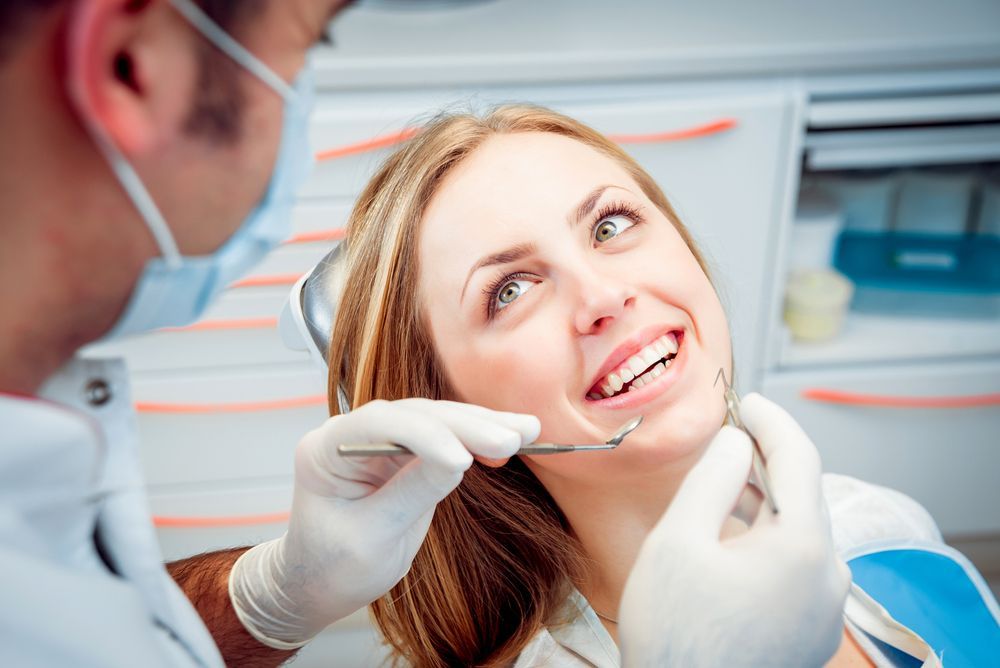Woman at dentist appointment, mouth open, dentist examining teeth with tools.