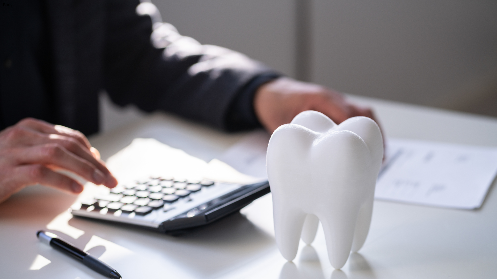 Person calculating dental costs with a tooth model on a desk.
