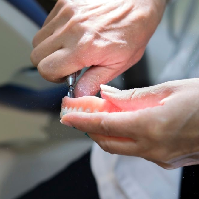 Person calculating dental costs with a calculator and clipboard near a large tooth model and laptop.