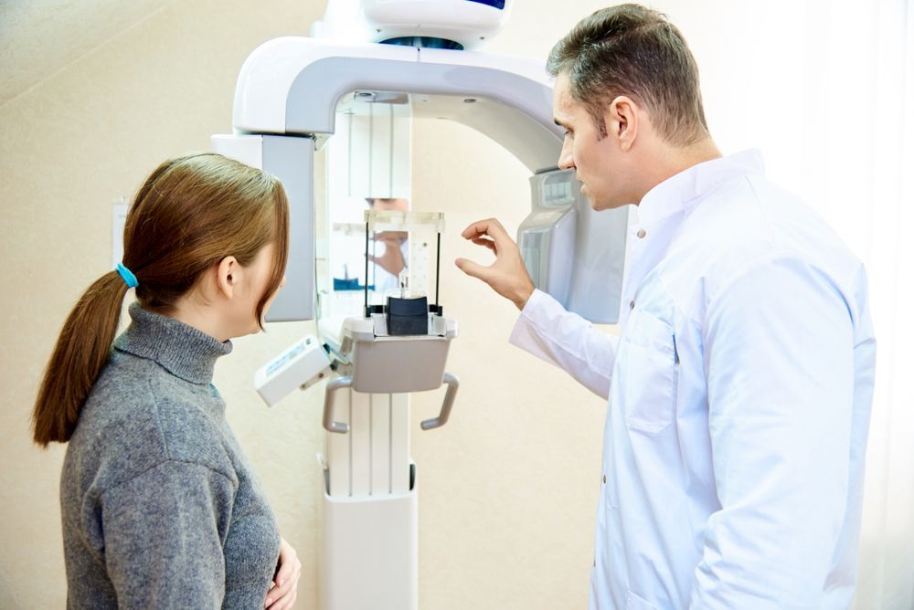 Dentist adjusting a panoramic X-ray machine with a patient in a dental office.