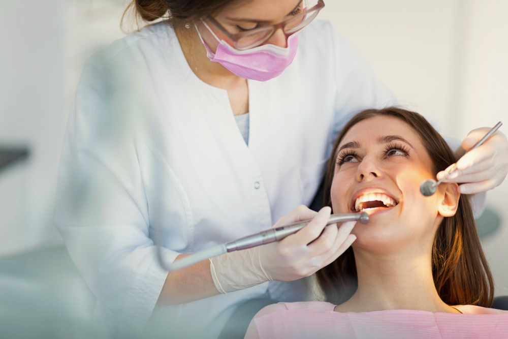 Dentist examining patient's teeth with tools in a clinic. Woman wearing mask and gloves.