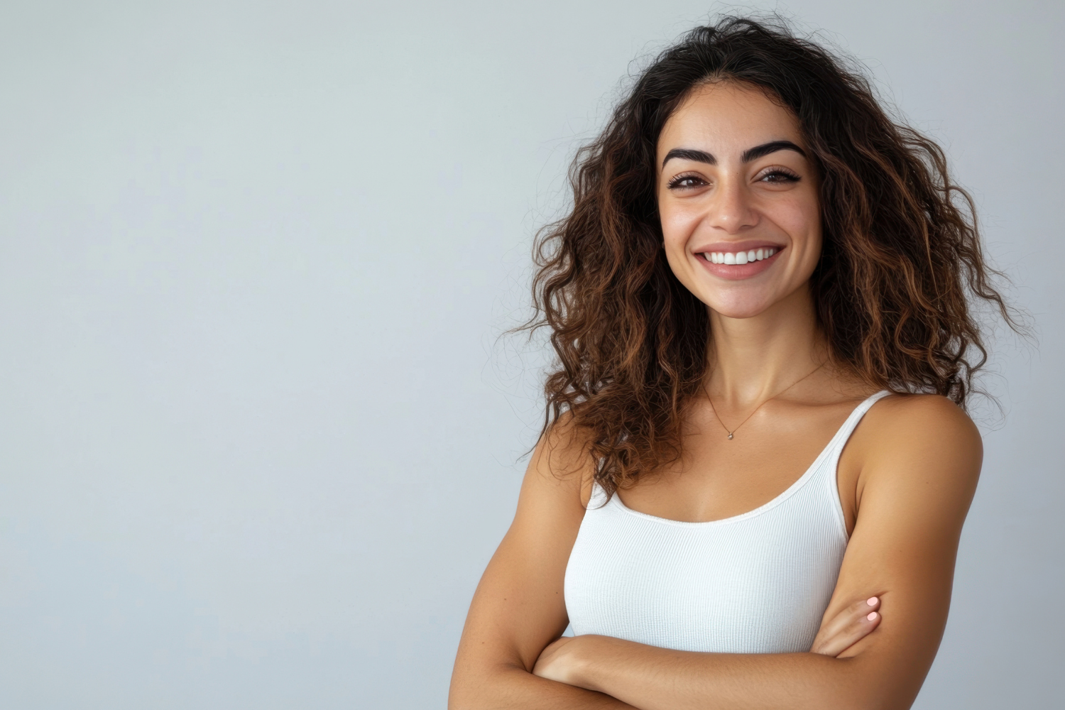 Woman with fair skin smiles widely, touching cheeks, against a light gray background.