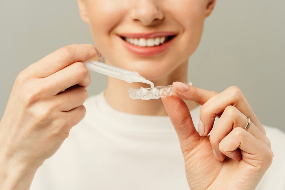 Woman smiling, applying liquid to a clear dental retainer.