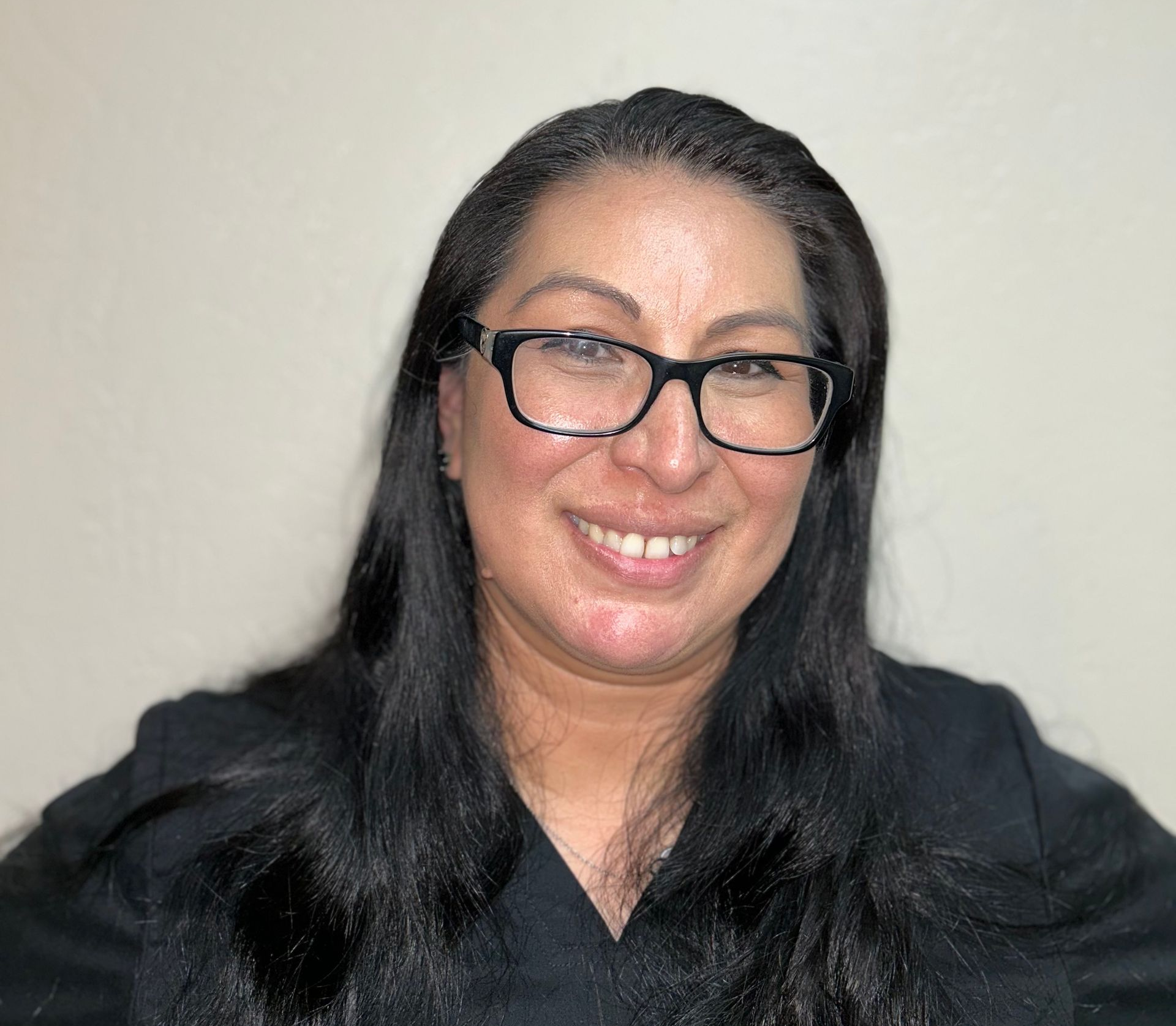 Woman with dark hair and glasses smiles in front of a black backdrop.