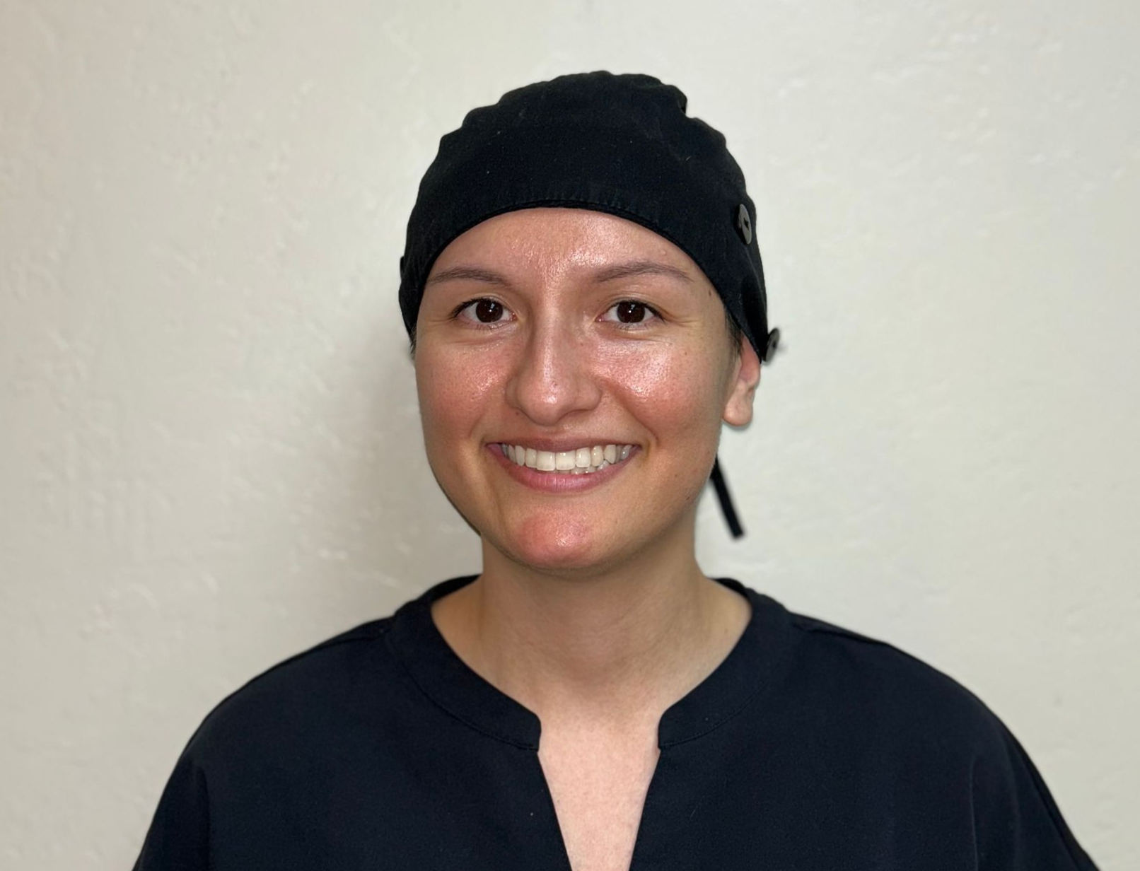 Woman with dark hair and glasses smiles in front of a black backdrop.