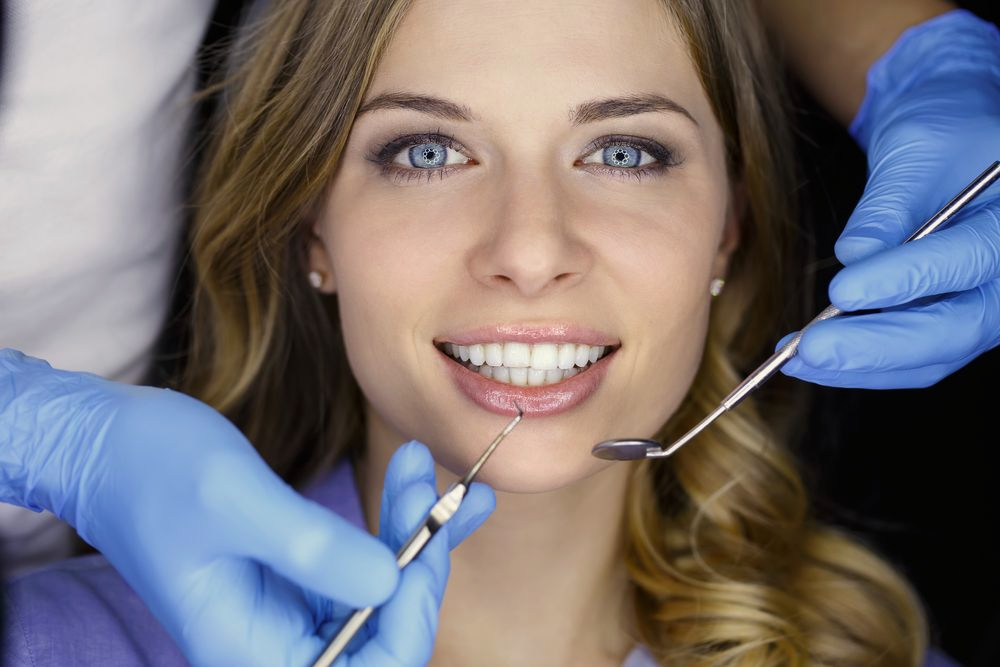 Woman in a dental chair; dentist's hands with tools in view.