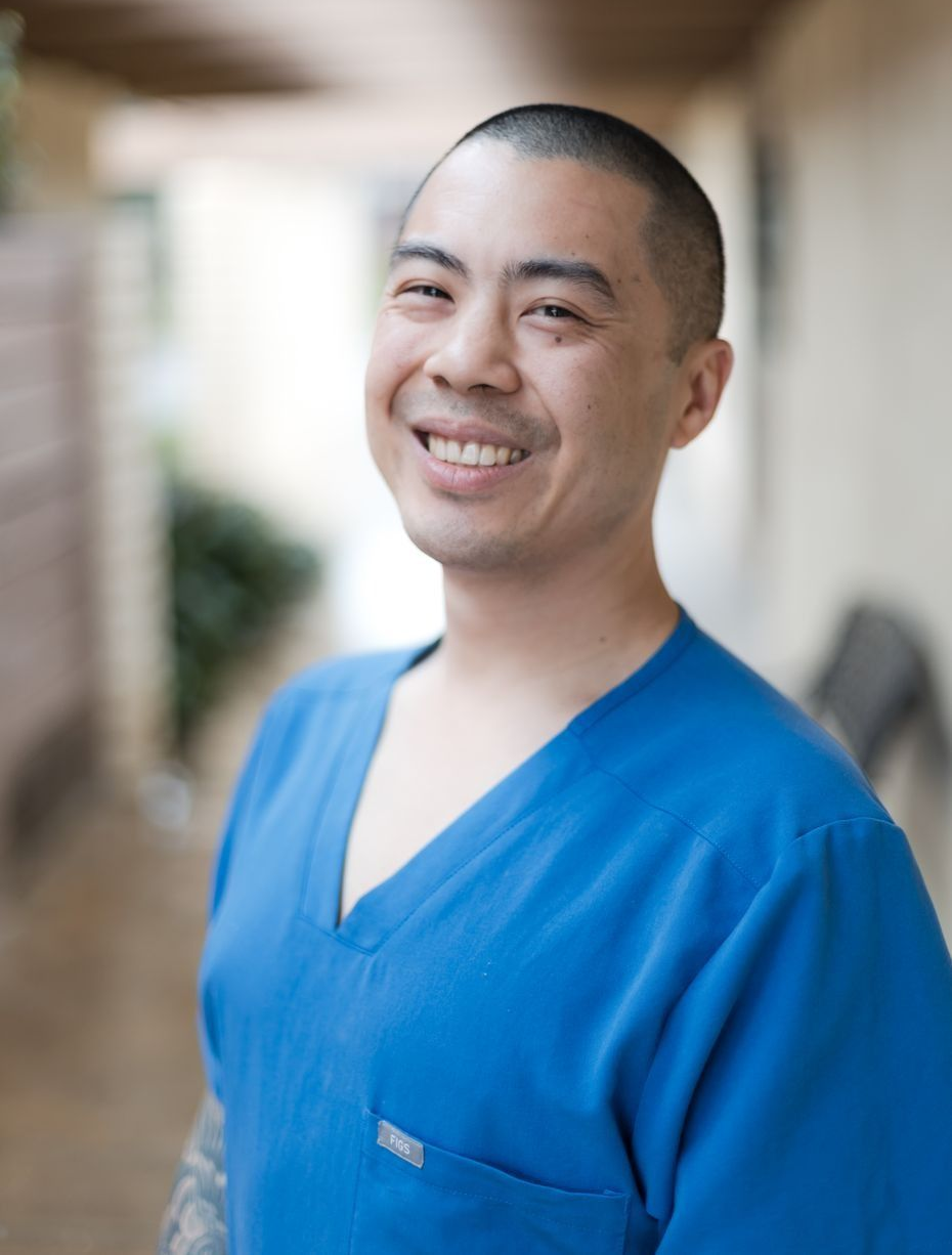 Person wearing blue scrubs smiles broadly, outside.