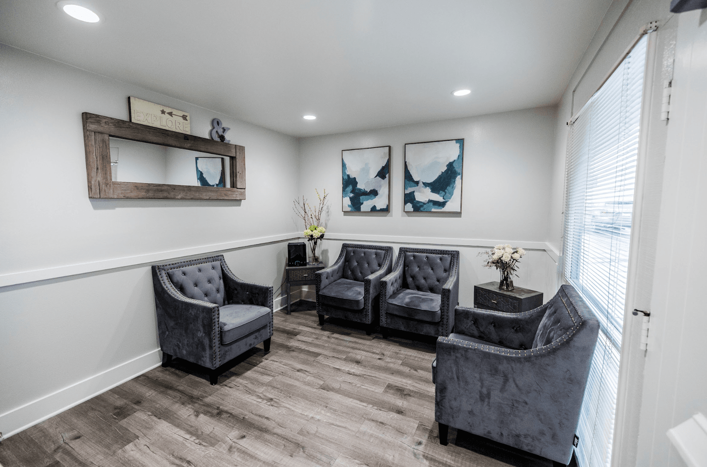 Waiting room with gray tufted chairs, artwork, mirror, and light wood-look flooring.