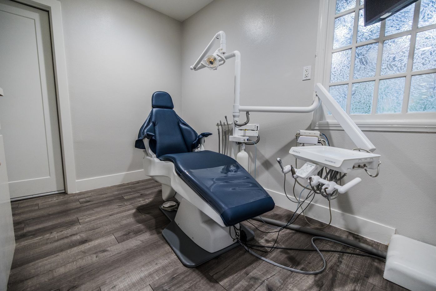 Dental chair in a light gray room, next to a window, with dental tools and equipment.