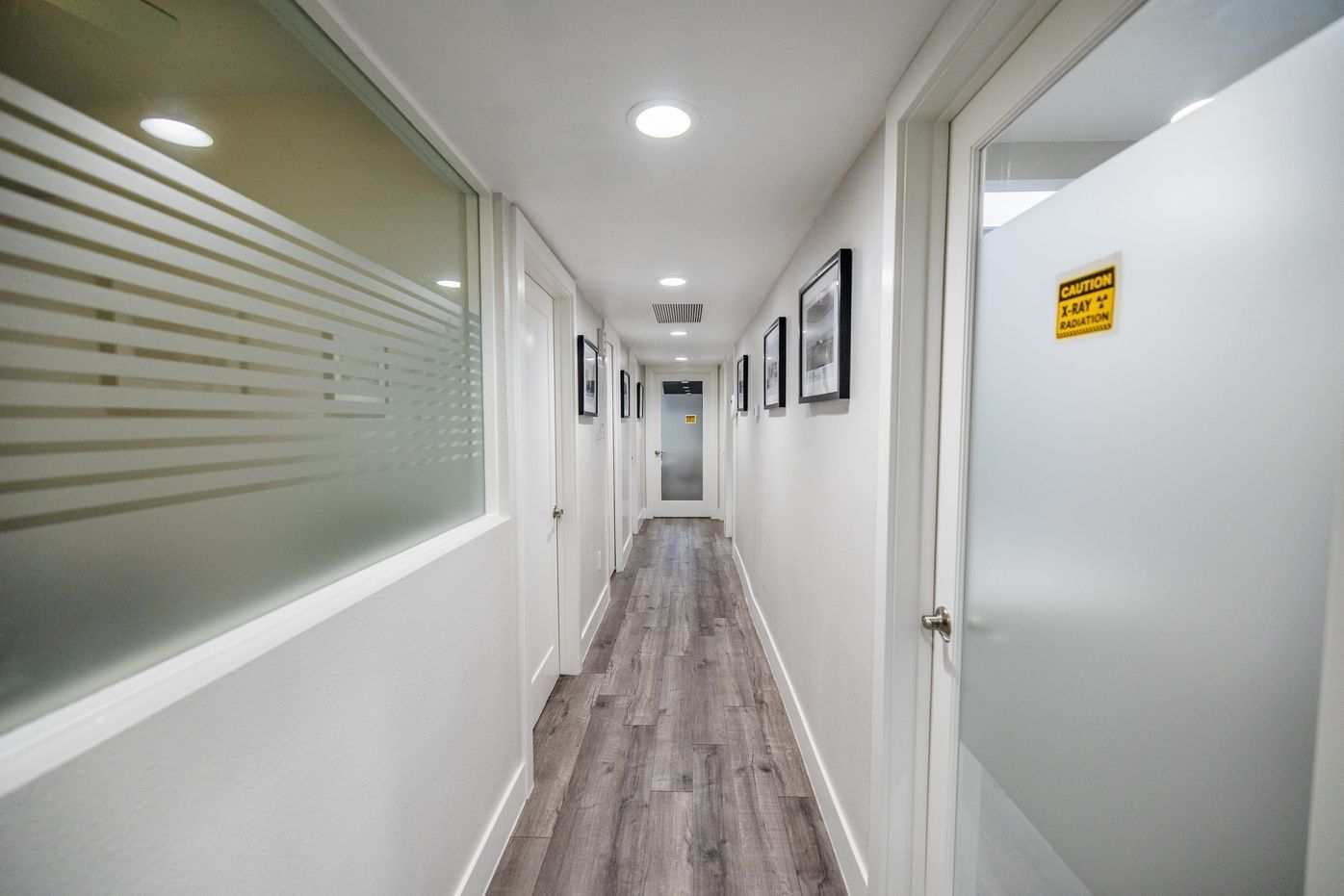 Long, narrow hallway in a white office with doors on both sides, wood-look flooring, and frosted window.